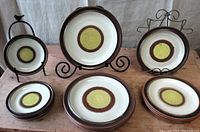 Set of 12 plates in the Potter's Wheel pattern by Denby arranged on a rustic wooden surface. Plates are displayed on stands and stacked to show different sizes.