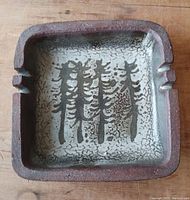 Front view of square ceramic ashtray showing interior glaze and abstract tree design.