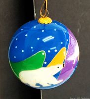 Side view of blue glass ornament showing a white polar bear against green, yellow, and purple shapes with white snowflakes. Shows gold hanging loop detail.