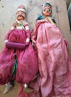 Two full-length puppets laid side by side on wooden surface, showing overall size and condition