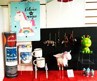 Photo showing unicorn figurine, two unicorn-themed coffee mugs, green and yellow Martian money bank, rhinoceros and ostrich Christmas ornaments, blue figurines, and novelty pens arranged on a black background