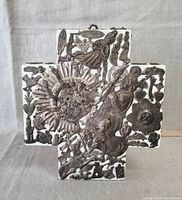 Front view of the white wooden cross decorated with numerous small metal milagro charms depicting hearts, animals, hands, and other symbolic shapes.