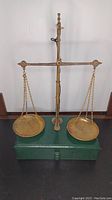 Full view of antique balance scale showing two brass pans on chains, brass post, and wooden base with drawer.