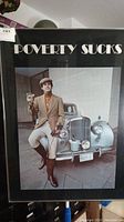 Full view of the framed art poster showing a man in vintage riding attire next to a classic car with text 'Poverty Sucks' on top.