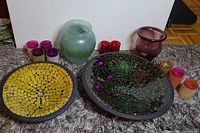 Photo showing two large painted mosaic center bowls, two art glass vases behind them, and multiple coloured glass candle holders surrounding them on a carpeted surface.