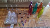 Wide view of assortment of stemware, mason jar mugs, colorful glass bottles, and shot glasses arranged on floor