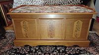 Full frontal view of the cedar blanket chest showing the upholstered bench seat and floral front panels.