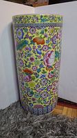 Full view of the porcelain umbrella stand showing colorful floral pattern on yellow background with a detailed border near the top