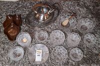 Two sets of MCM style clear glass dishware with rounded bubble pattern, several bowls and plates arranged on a carpet, along with a wooden divided tray.