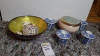 Photo of four blue and white Fukagawa lidded cups, beige ceramic urn, clam shell bowl with yellow interior, and shells