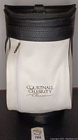 Front view of golf bag with white front pocket and logo, black leather top edge, and zipper pouch.
