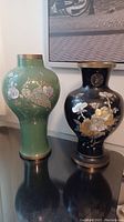 Two metal vases side by side: one green with bird and flower mother of pearl design, one black with floral mother of pearl design and brass rim/base.