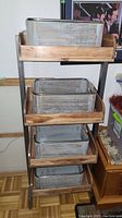 Front view showing full storage shelf with four metal baskets on wooden shelves.