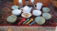 Lot contents displayed on carpet with teapot, apple bowls, spoons, glass bottles, and additional bowls and kitchenware