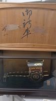 Close-up of the back wooden panel inside the display case showing Japanese characters and part of the miniature oxcart wheel.