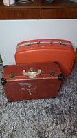 Two vintage suitcases on floor, red hard case and brown painted hard case.