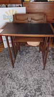 Front view of vintage wooden sewing table with black vinyl work top and folding legs.