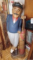 Full view of painted carved wood golfer sculpture with golf bag and clubs