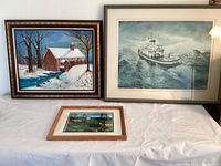 Three framed artworks displayed on a table: printed ship artwork, original oil of mill, smaller landscape print.
