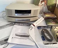 Bose Wave Music System front view showing unit with multi-CD changer, manuals, and remote control on white surface.
