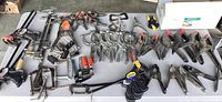 Wide view of various clamps including bar clamps, C-clamps, locking pliers, spring clamps, and black plastic clamps grouped on a table.