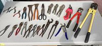 Top view of the full lot of hand tools spread out on a table showing cutters, pliers, wrenches and fence tools in various conditions.