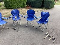 Shows 4 blue folding camping chairs with metal frames and 3 fishing poles with reels and cork handles on pavement outdoors