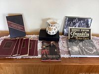 Wide view of all lot items on a wooden surface showing books, pitcher, and signage