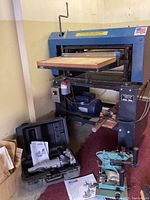 Front view of Woodmaster Tools planer on metal stand showing infeed table and outfeed table