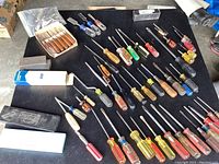 Wide view of assorted screwdrivers, chisels, and sharpening stones spread on black surface
