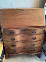 Front view of the closed secretary desk showing four curved drawers with metal handles and a drop-front writing surface with a lock.