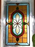 Full view of stained glass window hanging showing overall shape and color pattern with floral motif in center and amber-yellow background squares.
