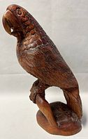 Photo showing full profile of the wooden parrot sculpture, highlighting detailed carving of feathers and perched stance.