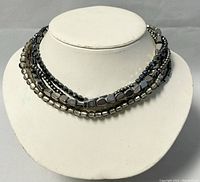 Five-strand silver-toned beaded choker with various bead shapes and sizes shown on bust display.