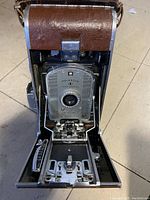 Front view of the vintage Polaroid 95B camera showing the open folding mechanism, lens plate, and leatherette body.