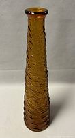 Front view of the tall amber glass genie bottle showing the textured wave pattern and flared lip.