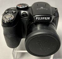 Front and angled side shot showing the Fujifilm FinePix S1800 camera with lens cap on.