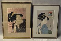Two framed Japanese geisha portraits, one silk print and one wood block print, side by side on a wall.