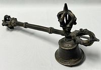 Bronze ritual bell photographed from side angle showing intricate vajra handle and bell body.