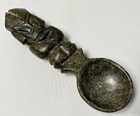 Side view of the stone spoon showing the figure carved on the handle and the bowl shape.