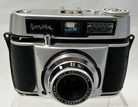 Front view showing lens, viewfinder window, and textured grip panels.