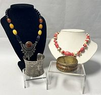 Four pieces of vintage costume jewelry: two necklaces and two bangles on display stands, showing overall lot composition and condition.