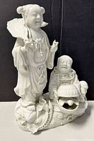 Front view of white Chinese porcelain figurine showing two joyful figures, one standing with fan and one seated holding bowl.