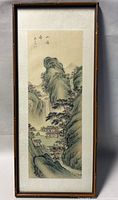 Framed vertical Chinese watercolour painting showing a mountainous rural village scene with traditional houses surrounded by cliffs and trees.