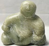 Front view of the green soapstone Inuit sculpture in seated pose showing general shape and surface details.