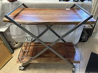 Front view of the wooden and metal bar cart showing the two tiers and caster wheels.