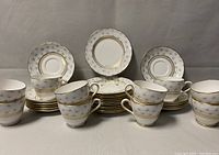 Photo of group of dessert plates stacked, teacups in front and saucers in the back, showing gold trim and thistle decorative pattern on white bone china.
