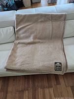Beige folded blanket placed on a white couch showing overall appearance and color tone.