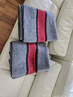 Two gray wool blankets with central red and black stripes folded on a couch, showing texture and color pattern.