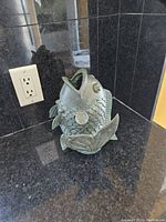 Front angle view of the cast iron koi carp statue placed on black granite surface with an electrical outlet in the background.